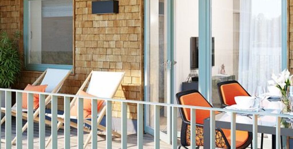 Balkong med sittgrupp och orange kuddar i nybyggt flerbostadshus.