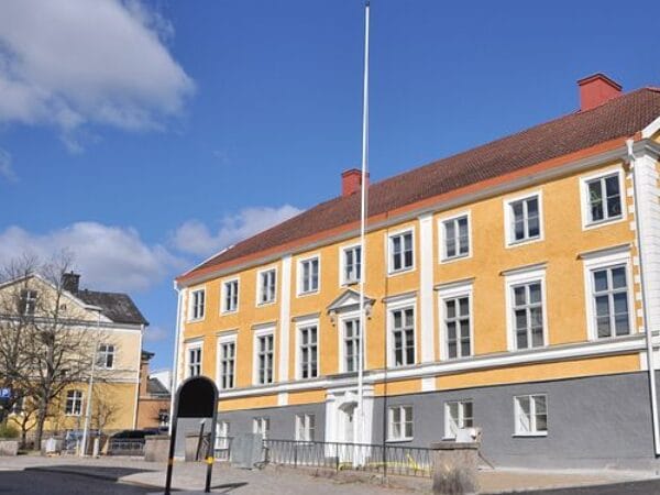 Gul byggnad med flaggstång i småstadsmiljö, blå himmel.