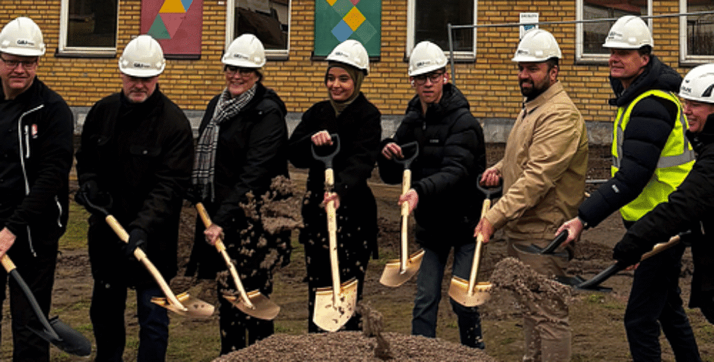 Grupp personer i bygghjälmar poserar med spadar vid byggstart.