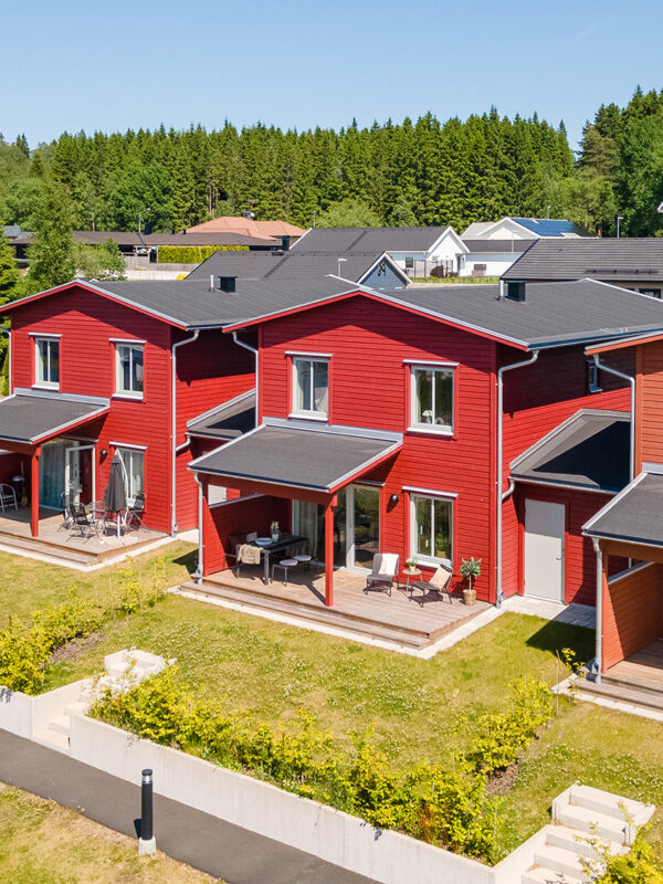 Flygbild över ett bostadsområde med röda trähus, där GBJ bostad har utvecklat moderna parhus i ett naturnära läge.