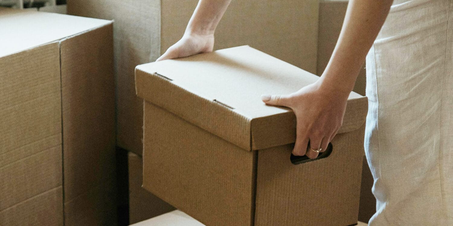 En person bär flyttkartonger i ett ljust hem – förmedlar känslan av nystart, inflytt och trygg bostadsresa med GBJ bostad.