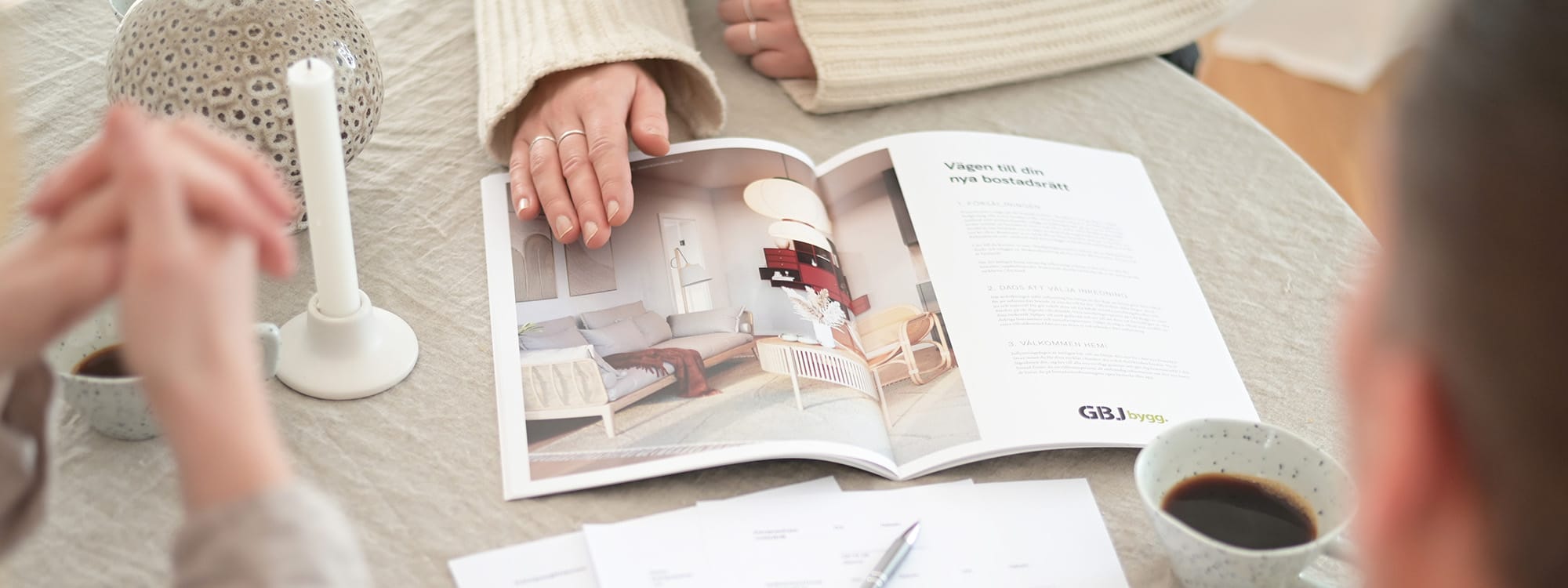 En person bläddrar i en bostadskatalog vid ett skrivbord, vilket illustrerar köpresan som många gör med GBJ bostad.