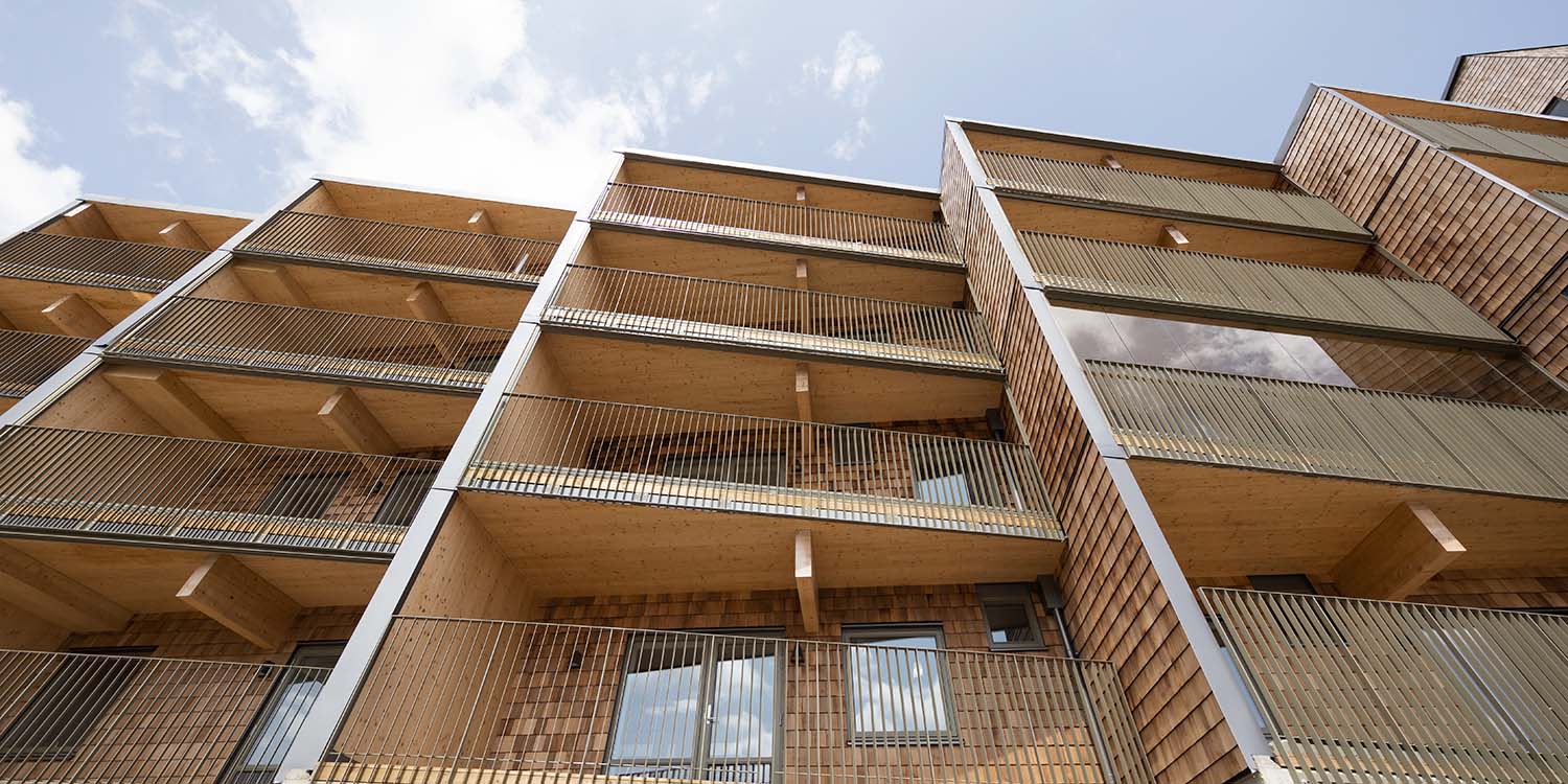 Uppåtriktad vy mot träbalkonger och fasaddetaljer – en del av en fastighet uppförd av GBJ Bygg som totalentreprenör.