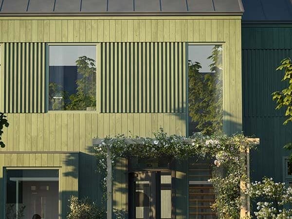 Nyproducerad bostadsrätt i Karlskrona med grön träfasad, uteplats och blommande entré i ett modernt och familjevänligt kvarter.