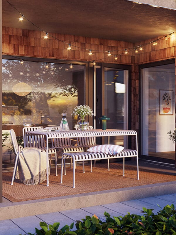 Kvällsbelyst uteplats med matmöbler under tak, omgiven av växtlighet, ett exempel på hur GBJ bostad i Stjärnhusen främjar sociala mötesplatser utomhus.