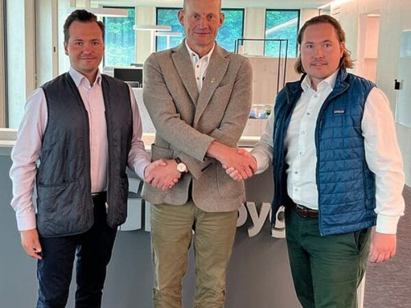 Tre personer poserar leende i kontorsmiljö med GBJ-logotyp i bakgrunden.