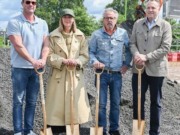 Fem personer med hjälmar och skopor poserar vid första spadtaget för nytt byggprojekt.
