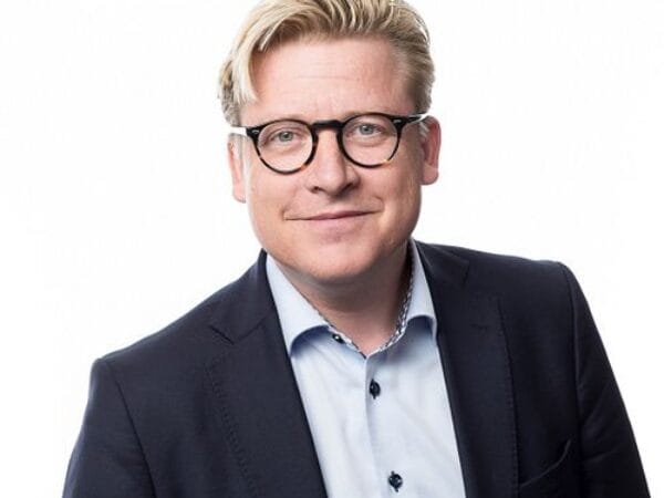 Porträttbild av man i kostym med glasögon mot vit bakgrund.