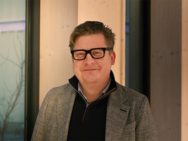 Tobias Abrahamsson, VD för GBJ Bostad AB, står leende i en modern träklädd interiör med stora fönster, en miljö som speglar företagets fokus på hållbarhet och stilren arkitektur.