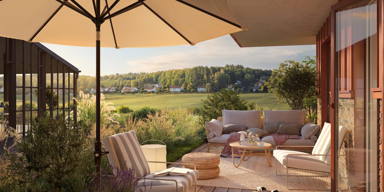 En uteplats med parasoll och bekväma sittmöbler vetter mot grönskande landskap, där boende kan koppla av i solen, och denna naturnära miljö är en del av det hållbara bostadskoncept som GBJ bostad utvecklat.