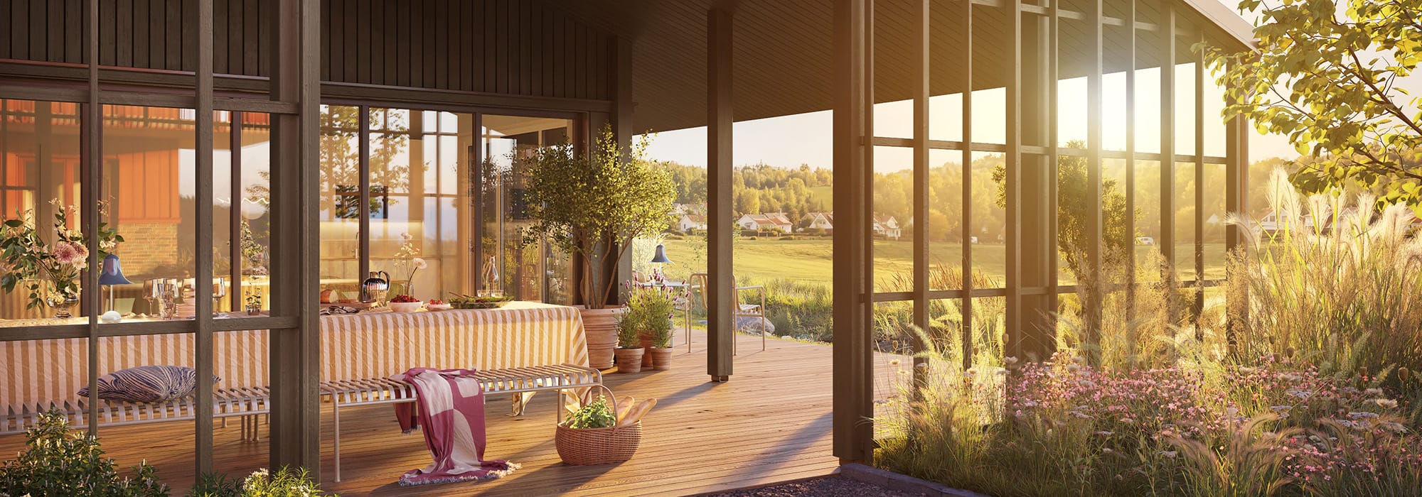 En stor träaltan med matplats, sittmöbler och grönska sträcker sig längs bostadens glasfasad med vy över öppna fält och bebyggelse. Ängsrum i Ytterby, utvecklat av GBJ bostad, erbjuder genomtänkta utemiljöer för både avkoppling och umgänge.